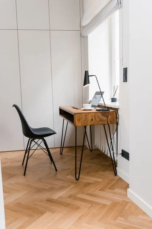 Simple budget home office with wooden desk, chair, laptop and desk lamp by a window